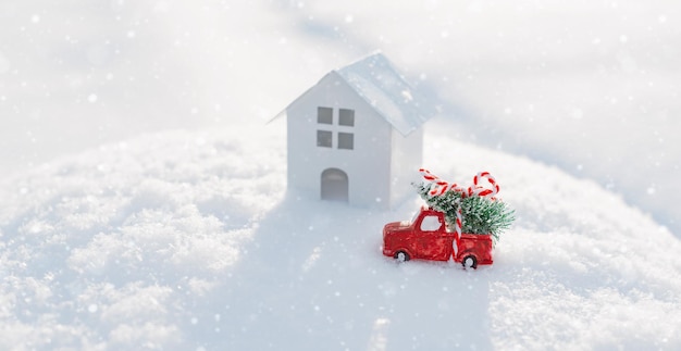 Carro decorativo de natal com uma árvore de natal na neve ao lado da casa