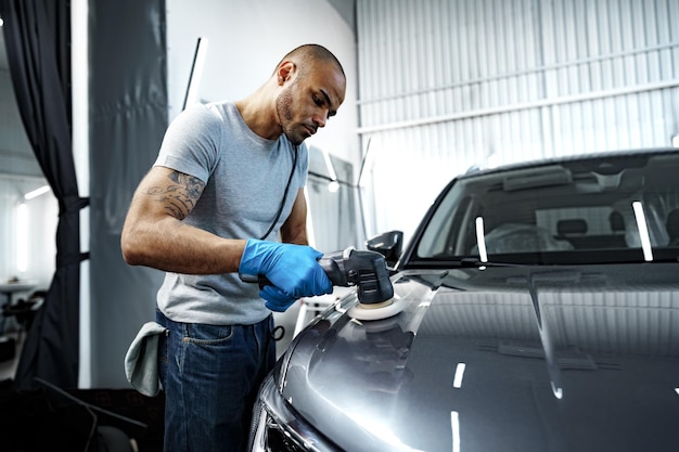 Carro detalhando as mãos masculinas com polidor orbital na oficina de reparação automóvel