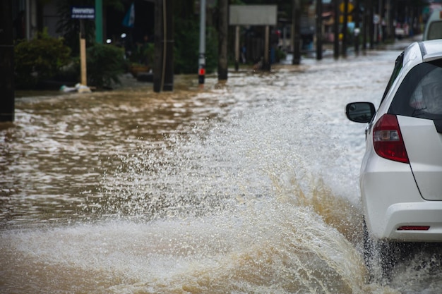 Foto carro dirigindo em estrada inundada com fluxo de água de inundação na estrada após chuva forte e ondas de tempestade