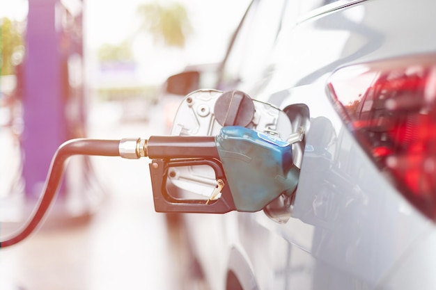 Carro enchendo combustível no posto de gasolina Foco no bico de combustível e desfoque o fundo da luz do dia