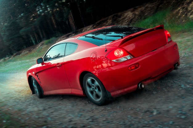 Carro esportivo vermelho se move em terreno acidentado com faróis retrovisores