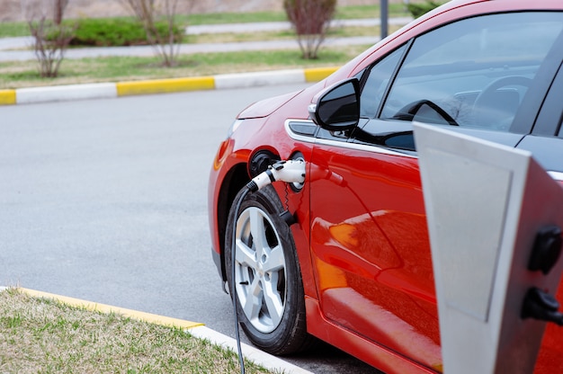 Carro ev ou carro elétrico vermelho na estação de carregamento com o cabo de alimentação