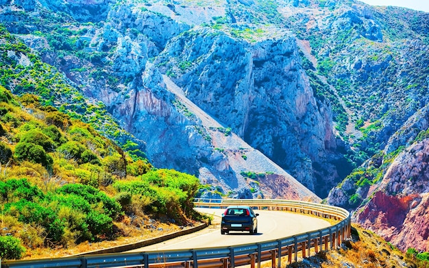 Carro na estrada em Buggerru na ilha da Sardenha no verão de Itália. Transporte de condução na estrada da Europa. Ver férias na auto-estrada. província de Cagliari. Montanhas no fundo. Mídia mista.