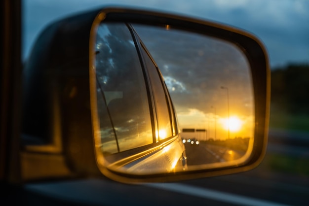 Foto carro no pôr do sol da estrada no reflexo do espelho do carro