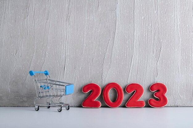 Carro pequeño y números 2023 sobre fondo claro Compras para el nuevo año Descuentos de Año Nuevo