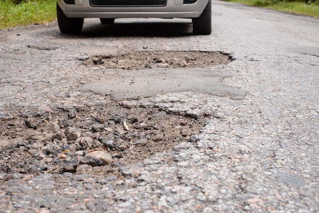 Carro perto de muitos buracos profundos e perigosos na superfície do asfalto