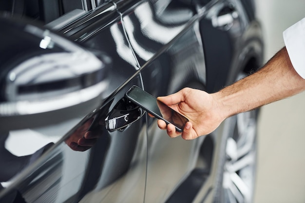 Carro preto Vista aproximada da mão do homem que segura o telefone com rótulos e ícones Concepção de controle remoto