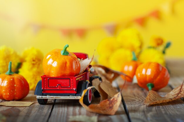 Carro rojo con calabazas en mesa de madera con flores amarillas y hojas secas sobre fondo amarillo. Concepto de postales de otoño y día de acción de gracias.