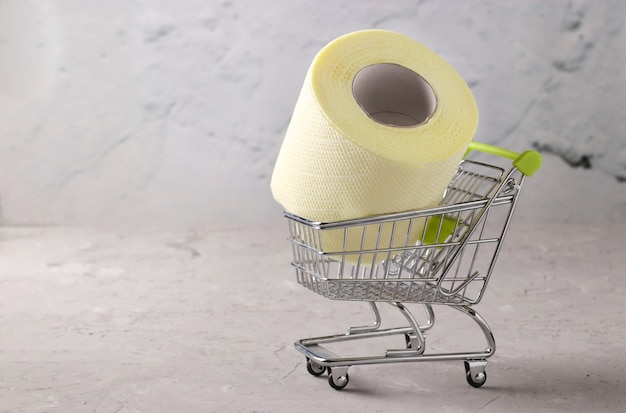 Carro de supermercado con rollo de papel higiénico suave sobre fondo gris, pandemia de Covid-19, aumento de la demanda inesperada, espacio de copia