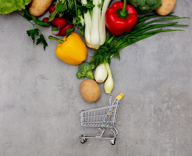 Carro de supermercado y verduras en una mesa