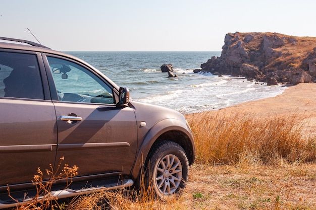 carro SUV na costa rochosa do mar com uma praia de areia e grama queimada pelo sol Viagens e turismo