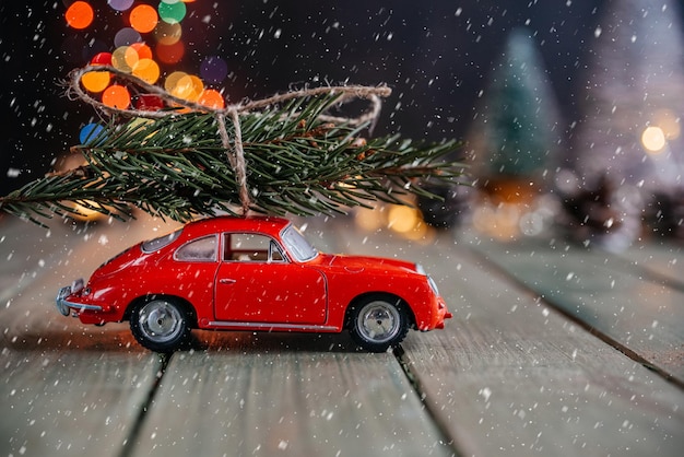 Carro vermelho em miniatura com árvore de abeto no fundo de natal com bokeh colorido de luzes de natal