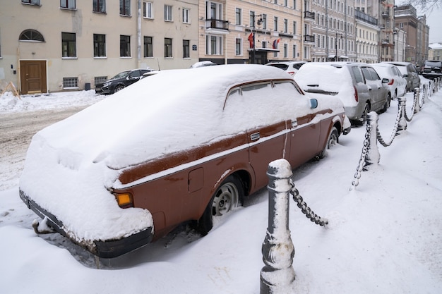 Carros estacionados cobertos de neve em uma estrada de neve suja após a queda de neve. Mau clima de inverno, aumento da precipitação e conceito de níveis de neve