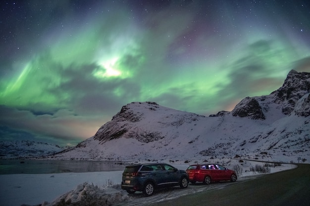 Foto carros estacionados em estrada rural com aurora boreal no céu em lofoten, ilhas