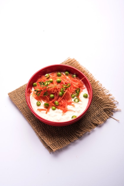 Carrot Raita ODER Gajar Koshimbir mit Quark, Grün, Erbsen, Chili und Koriander. Serviert in einer Schüssel über stimmungsvollem Hintergrund. selektiver Fokus