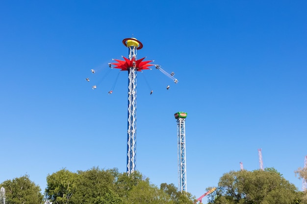 Carruseles extremos altos contra el cielo azul sobre árboles verdes