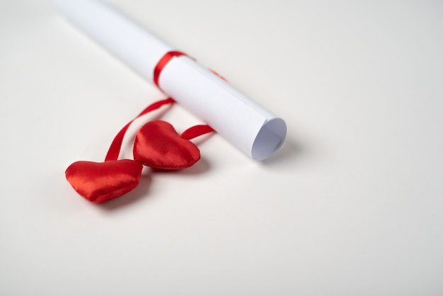Carta de amor enrollada del Día de San Valentín atada con una cinta roja con corazones rojos sobre el fondo claro (blanco)