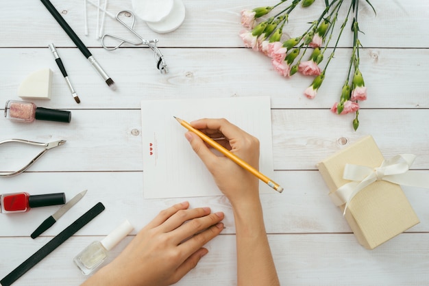 Carta de amor de San Valentín sobre fondo de madera. Café, dulces y galletas en forma de corazón de terciopelo rojo. Manos femeninas con esmalte de uñas rojo