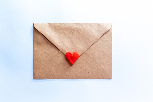 Foto carta de amor en un sobre artesanal con corazón de arcilla roja sobre fondo azul claro.