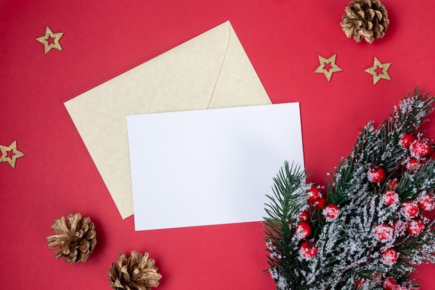 Foto carta blanca en blanco a santa claus con página vacía y sobre dorado en la vista superior de fondo rojo con rama de abeto y bayas rojas con conos de pino y estrellas doradas