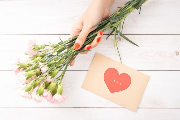 Carta de amor de dia dos namorados em fundo de madeira. envelope marrom, nota rosa e caixa de presente na mesa. mãos femininas com esmalte vermelho