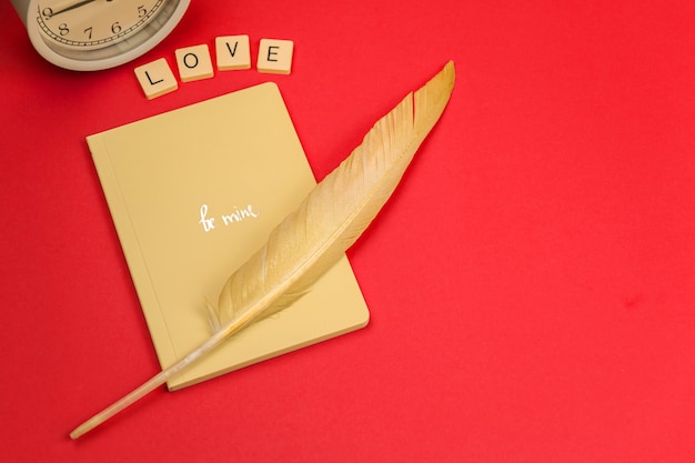 Carta de amor, envolva caderno com pena amarela, conceito de Dia dos Namorados, fundo vermelho e copie a foto do espaço