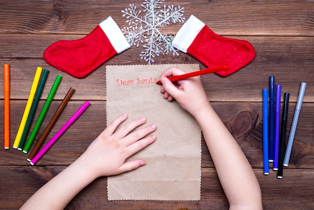 Carta infantil para o papai noel. menina escreve uma carta com canetas de feltro coloridas sobre uma mesa de madeira