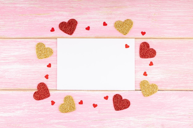 Cartão branco em branco com corações feitos à mão têxteis no fundo rosa de madeira