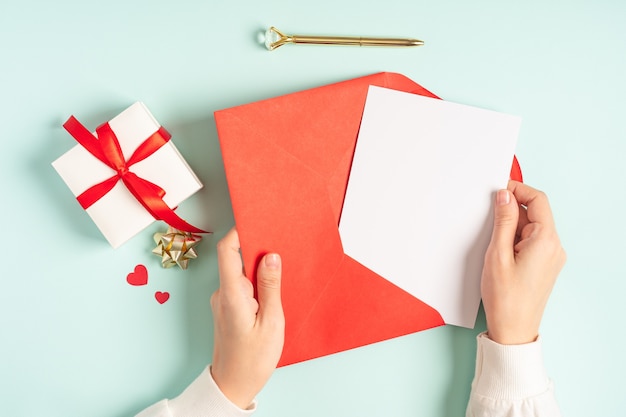 Cartão branco em branco com envelope de papel vermelho nas mãos