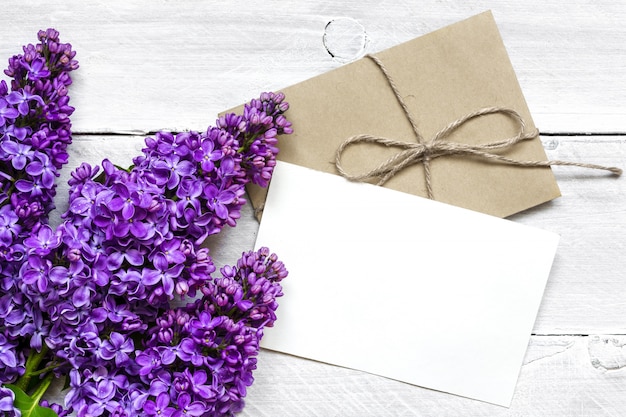 Foto cartão branco em branco e envelope com flores lilás sobre a mesa de madeira branca