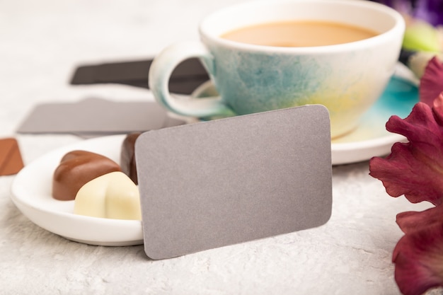 Cartão cinza com uma xícara de café, bombons de chocolate e flores de íris na superfície cinza.