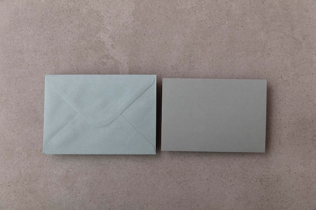 Cartão cinza em branco com modelo de envelope de papel cinza simulado em um fundo de concreto