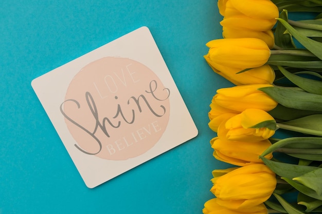 cartão com a inscrição Love Shine Believe tulipas amarelas em fundo azul