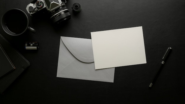 Cartão com envelope cinza na mesa de escritório escuro com câmera digital e material de escritório