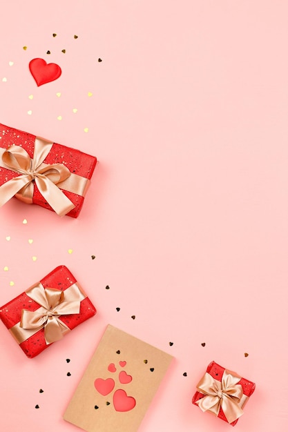Cartão criativo do Dia dos Namorados com decorações vermelhas e caixas de presente, confetes de coração dourado no fundo rosa, espaço de cópia, vista superior