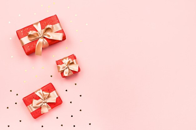 Cartão criativo do dia dos namorados com decorações vermelhas e caixas de presente, confetes de coração dourado no fundo rosa, espaço de cópia, vista superior