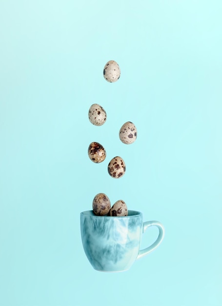 Cartão criativo mínimo de Páscoa Ovos de codorna e caindo no copo azul sobre fundo azul claro Vista superior