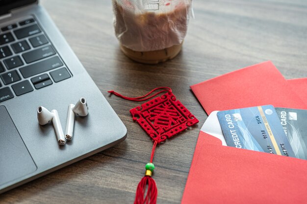 Cartão de crédito em envelope vermelho, fone de ouvido no computador laptop com o texto em chinês bênçãos escritas nele é uma primavera com café isolado em mesa de escritório de fundo de madeira para bônus de ano novo chinês