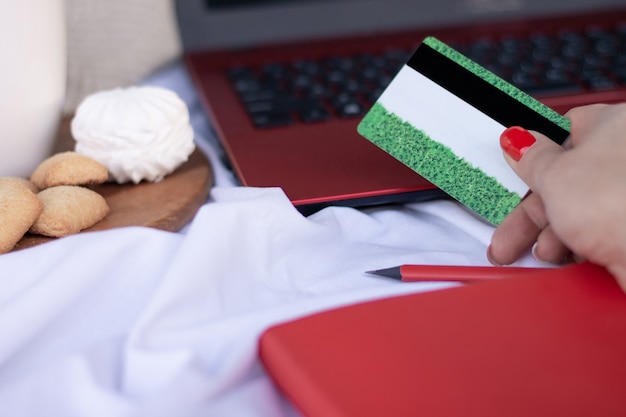 Foto cartão de crédito em mãos perto do teclado de um laptop vermelho