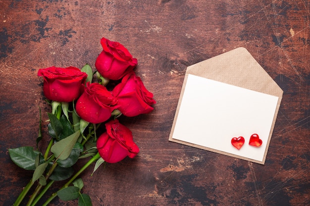 Cartão de dia dos namorados Buquê de flores rosas vermelhas e envelope de artesanato com corações vermelhos em um fundo de madeira vintage