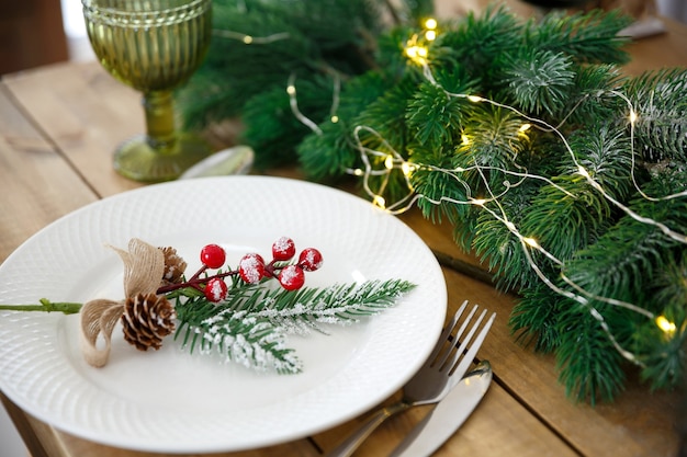 Cartão de felicitações. Mesa de madeira com decoração de natal. Configuração de mesa com utensílios. Decoração festiva de ramos de abeto e guirlandas.