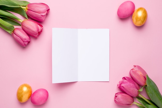 Cartão de felicitações, ovos de Páscoa e flores tulipas em uma superfície rosa