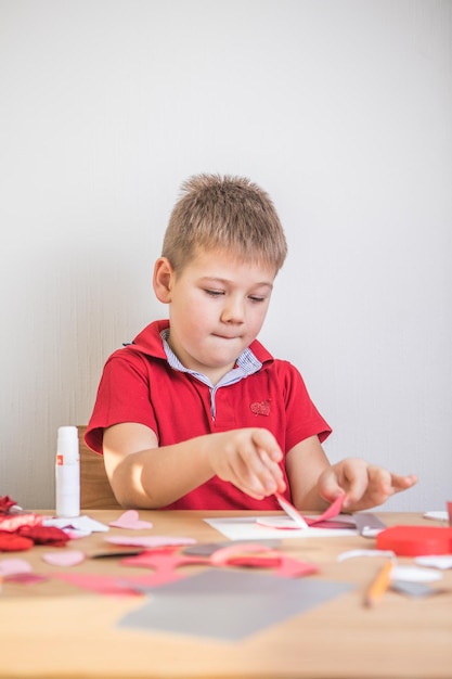 Cartão de férias DIY com coração de papel vermelho, símbolo do amor. Garoto garoto faz o dia das mães, dia dos namorados, cartão de felicitações. Hobby, conceito de arte infantil, presente com suas próprias mãos, ideias DIY para crianças