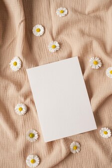 Cartão de folha de papel em branco com botões de flores de camomila de espaço de cópia de maquete e pano de musselina bege neutro modelo de convite de casamento estético mínimo vista superior plana