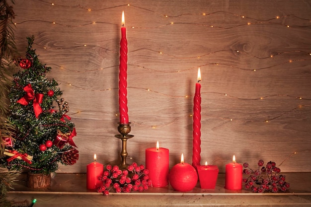 Foto cartão de natal com velas vermelhas brilhantes na prateleira da lareira perto da árvore de natal