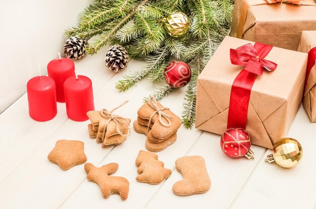 Cartão de Natal e ano novo com uma composição de presentes, enfeites para árvores de Natal e galhos, biscoitos de gengibre em um fundo branco de madeira