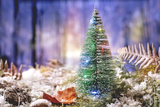Cartão de Natal ou ano novo com árvore de Natal decorativa iluminada em musgo coberto de neve com floresta de inverno no fundo. Atmosfera de férias de natal