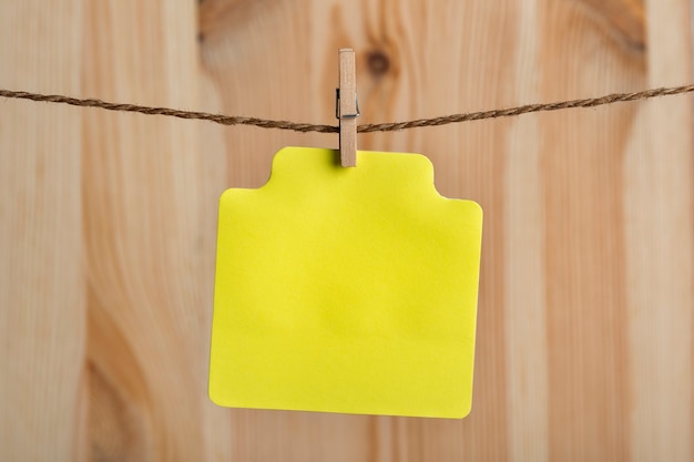 Cartão de papel amarelo em branco com prendedor de roupa na corda. Lugar para o seu texto. Copie o espaço. Fundo de madeira.