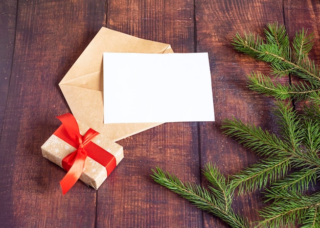 Cartão de papel branco em branco em um envelope marrom de papel artesanal em uma velha mesa de madeira em um estilo de natal cones de ramos de abeto na mesa