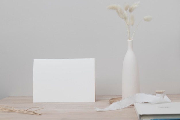 Cartão de papel em branco, maquete de cartão. decoração com rabo de coelho seco, vista frontal, grama de rabo de coelho linda em vaso na mesa de madeira e fundo de parede de cimento bege